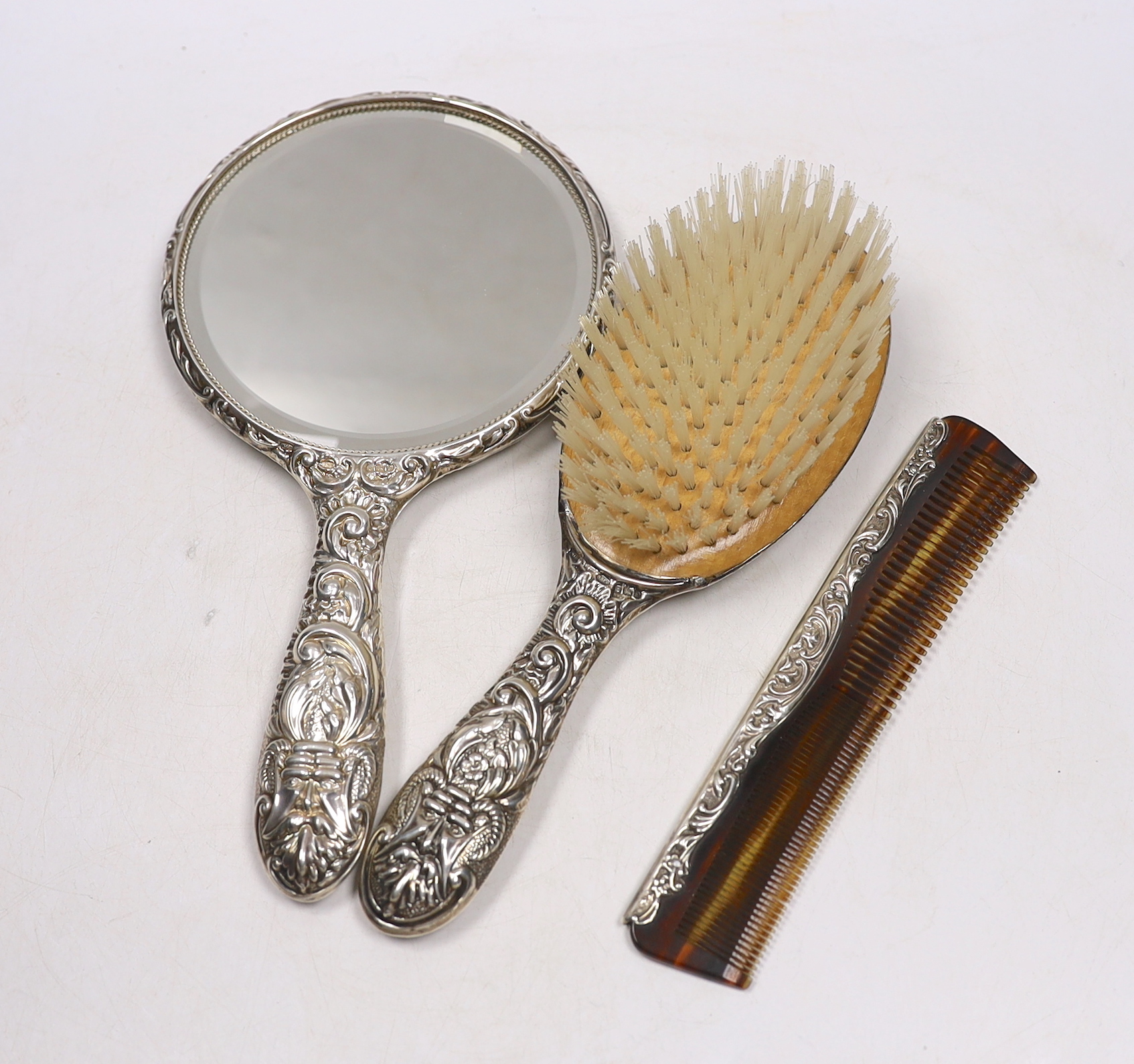 A modern repousse silver mounted hand mirror, two brushes and a comb.